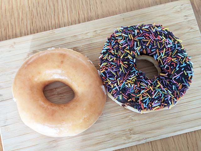 クリスピー・クリーム・ドーナツ 福袋 2024に入っている「フォーチュン 干支 ダズン（12個）1箱」のドーナツ「オリジナル・グレーズド®」と「チョコ スプリンクル」がテーブルに並んでいる様子。