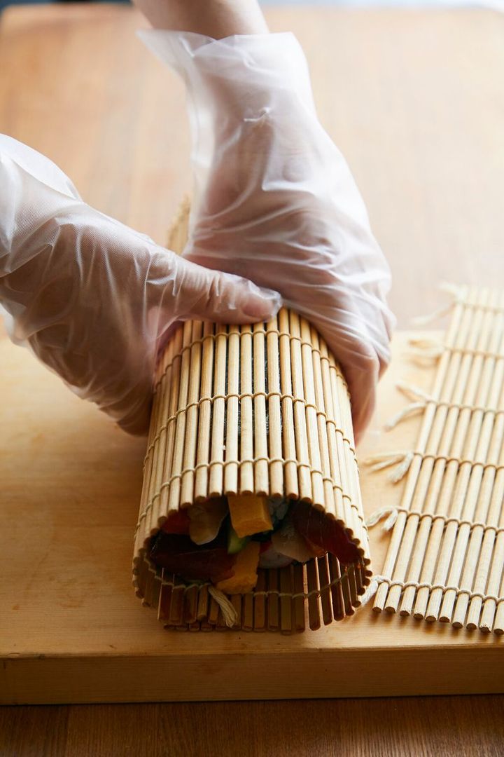 手前の巻きすを持ち上げて一周したら、左手で太巻きをぎゅっと押さえ、形を整えて。