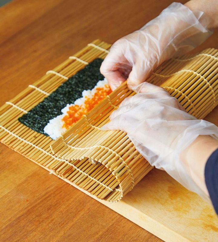 左手太巻きを押さえては、右手で巻きすを向こう側へ引っ張る、を繰り返して巻き進めて。