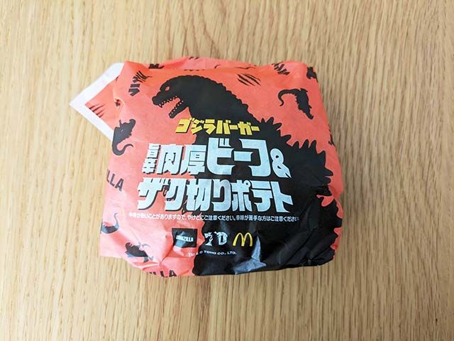 ゴジラデザインの包装紙に包まれた【マクドナルド】新商品「旨辛肉厚ビーフ&ザク切りポテト」