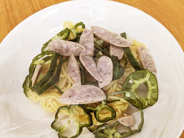 【カルディ新商品】「キムチナポリタン」の麺が耐熱皿に入れられ、薄切りのウインナー、輪切りのピーマンがトッピングされ、ラップをかけられている様子