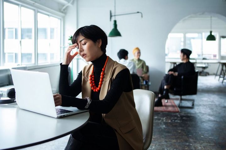 オフィスでノートパソコンを使用し、ため息をついている女性