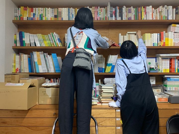 安西水丸事務所の本棚で学芸員が書籍をチェックする様子