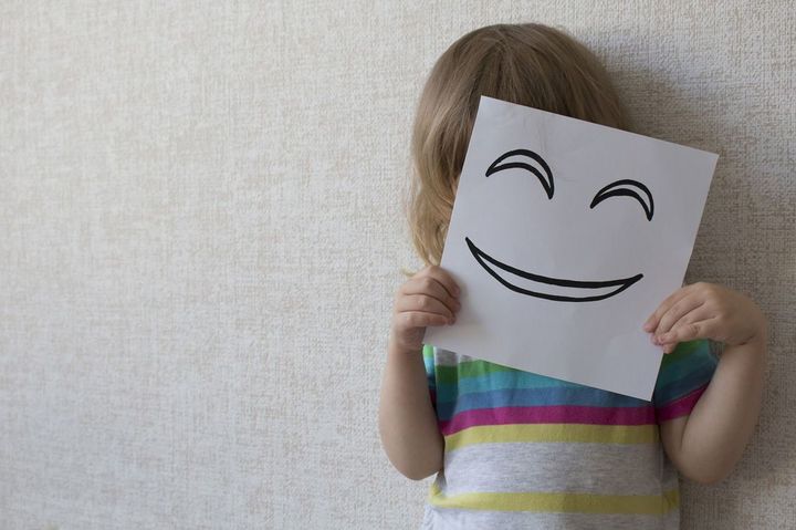笑った顔が描かれた紙で顔を隠す子ども