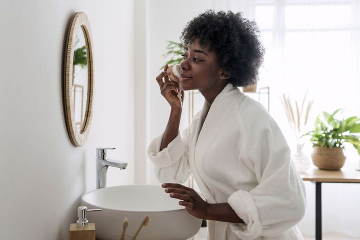 smiling woman massaging face looking in mirror at home