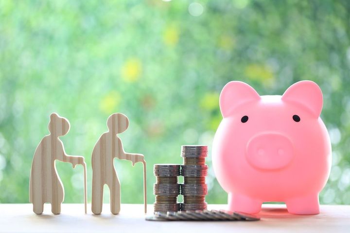 緑の自然を背景にシニア夫婦の人形と積み上げられた硬貨、豚の貯金箱