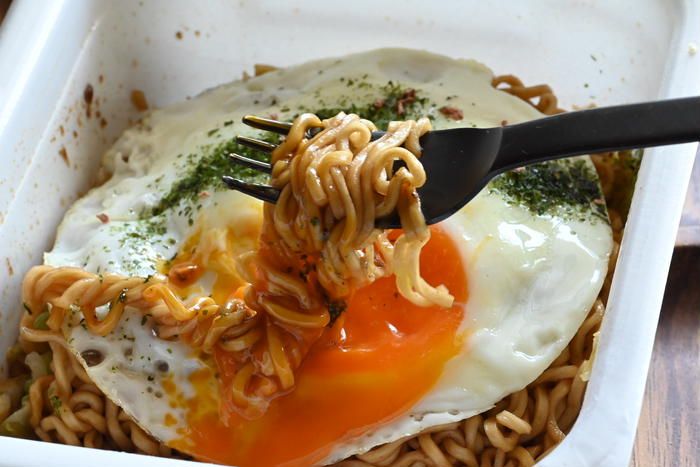 目玉焼きがのったカップ焼きそばをフォークで箸上げしている様子