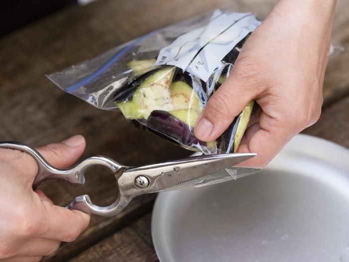 ナスの入ったジッパー付き保存袋の角をハサミで切る様子