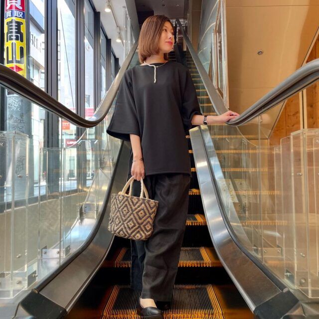 ブラックの半袖プルオーバーとブラックのリネンイージーワイドパンツと籠バッグのようなミニトートバッグ、パールネックレス