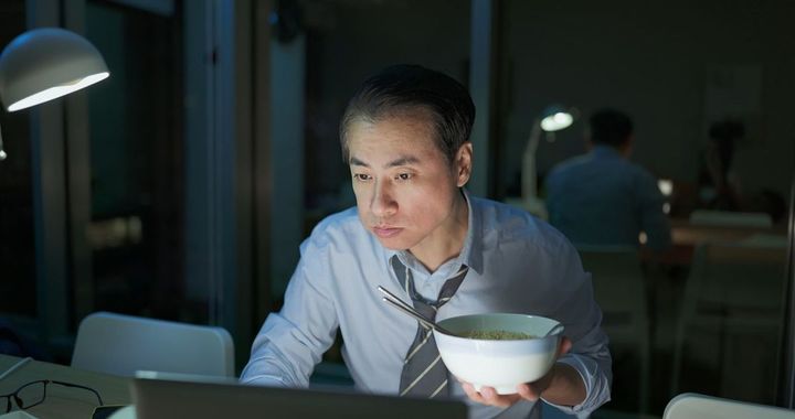 夜間にオフィスでラーメンを食べながら働く男性