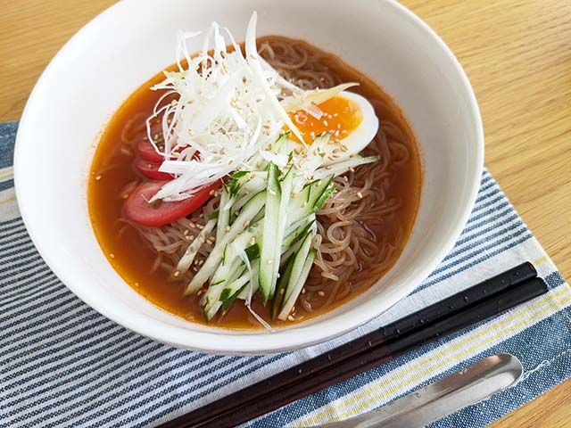 調理された業務スーパー「トマト冷麺」がテーブルに置かれている様子。トッピングはきゅうり、白髪ネギ、ゆで卵、白ごま、トマトの輪切り