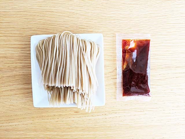 業務スーパー「トマト冷麺」の袋の中に入っている乾麺と別添えスープがテーブルに並んでいる様子