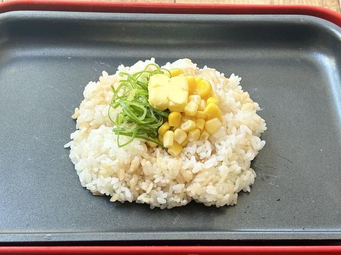 ホットプレートの中央に置かれたごはんのくぼみににコーン缶と小口ねぎバターをのせたところ