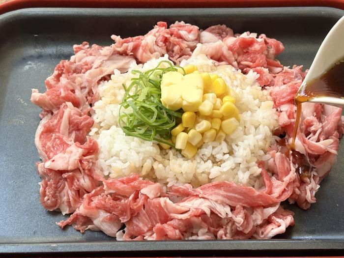 ホットプレートの上のごはんの周りに 牛肉を盛り付け焼肉のたれをかけているところ