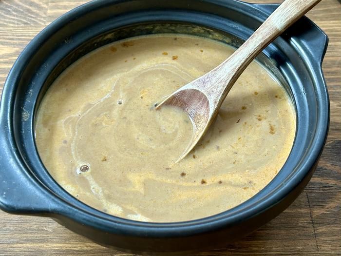 土鍋にレトルトカレーで作ったクリームカレースープをスプーンで混ぜているところ