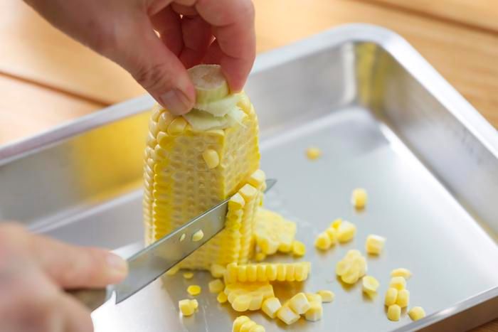 トウモロコシを半分に切って、実をそいでいる様子
