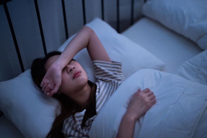 腕で目を覆ってベッドで眠ろうとする女性