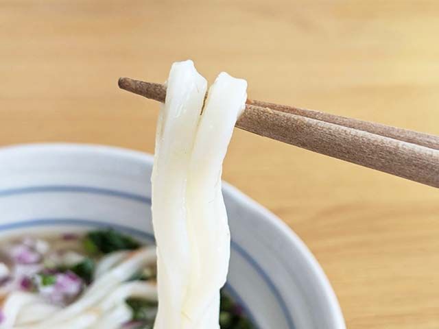 カルディ「麺にかけるだけ 鮭レモンつゆ」をかけたうどんの麺を箸で持ち上げているところ