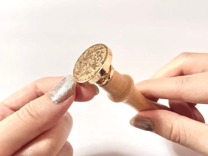 ダイソー「シーリングスタンプ用 ハンドル」を手に持ち、「シーリングスタンプ用 スタンプヘッド」を取りつけた様子