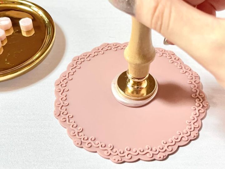 「シーリングスタンプ用 シリコーンマット」にたらした「シーリングワックス 粒タイプ」リッチピンクカラーを「シーリングスタンプ用 ハンドル」と「シーリングスタンプ用 スタンプヘッド」を使いプッシュする様子