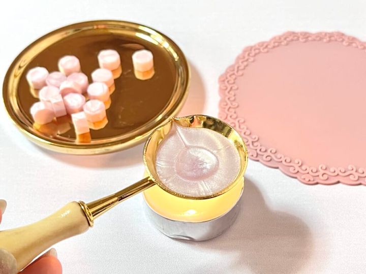 ダイソー「シーリングスタンプ用 スプーン」に「シーリングワックス 粒タイプ」リッチピンクカラーを入れ、「ソイキャンドル 9個入」でワックスを溶かす様子