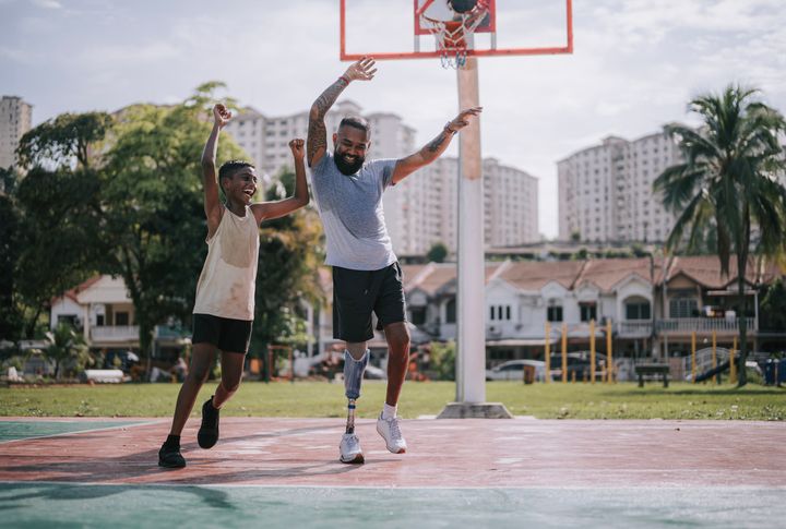 義足をつけたアジア系インド人の父親が、息子とバスケットボール場にいる