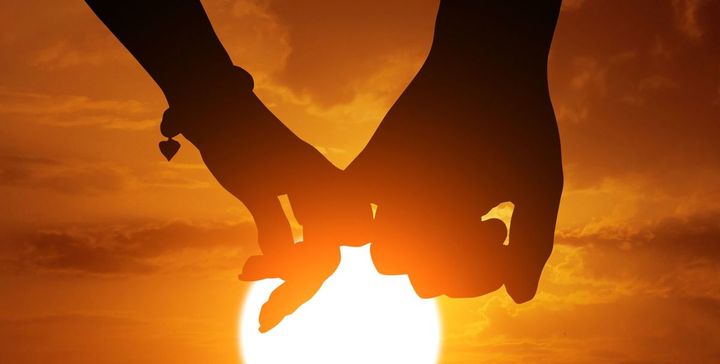 夕暮れ時に手をつないでいるカップルの手のシルエット