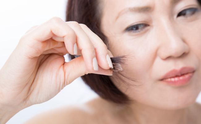 毛先を悩ましげに見る女性のイメージ