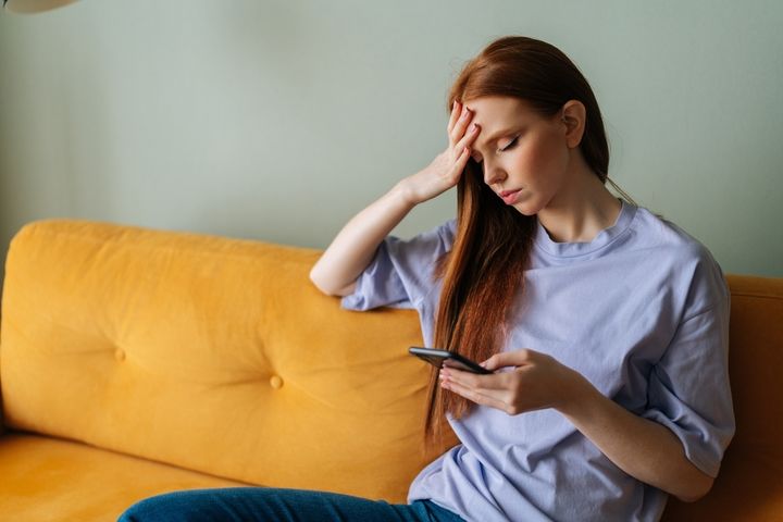 ソファでスマートフォンを見ながら残念そうな女性