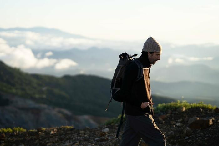 ROUVERのニットを着て山を歩く男性