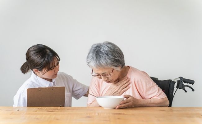 誤嚥に苦しむ高齢者と食事介助するヘルパー