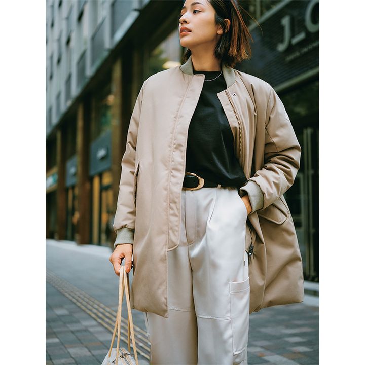 黒のトップスとベージュのパンツにピレネックスのノンキルトデザインのベージュダウンを羽織ったコーデ