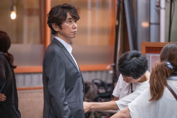 入店前のユースケ・サンタマリアさん。役柄の生まじめなキャラクターが伝わる、ダークスーツ姿です。