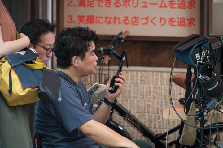 トランシーバーで店内とコミュニケーションする監督の北畑龍一さん（手前）と一緒にモニターを見つめる脚本の田口佳宏さん。