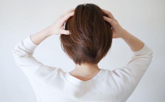 頭をかきむしる女性の後ろ姿のイメージ