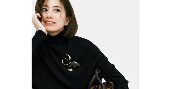 黒のタートルネックの胸元に地金系のモチーフブローチを重ねづけ