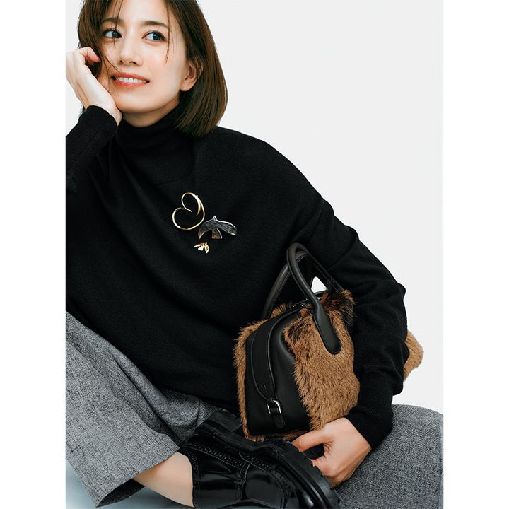 黒のタートルネックの胸元に地金系のモチーフブローチを重ねづけ