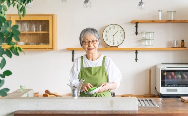 家のキッチンでお皿洗いをするシニア女性