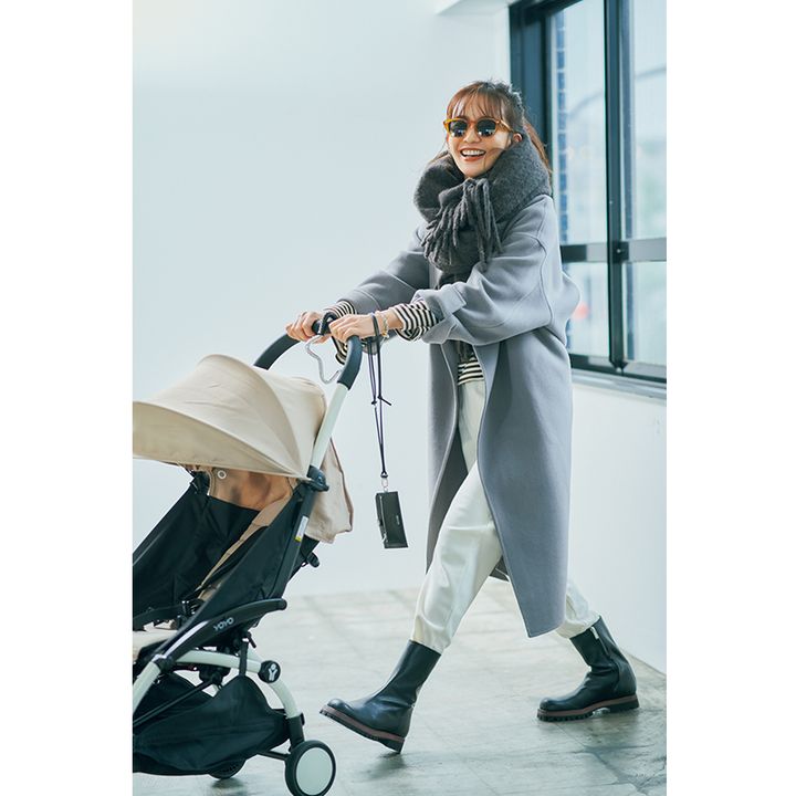 グレーのロングコートとマフラーに白のジョグパンツ、足元はブーツの暖かコーデでベビーカーを押すママモデル