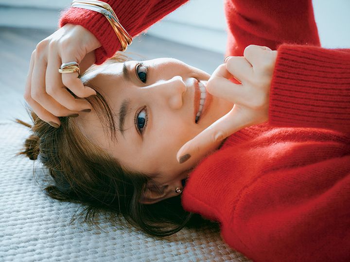 赤いニットを着てカルティエのトリニティリングとブレスレットをつけて横たわる東原亜希さん