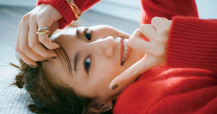 赤いニットを着てカルティエのトリニティリングとブレスレットをつけて横たわる東原亜希さん