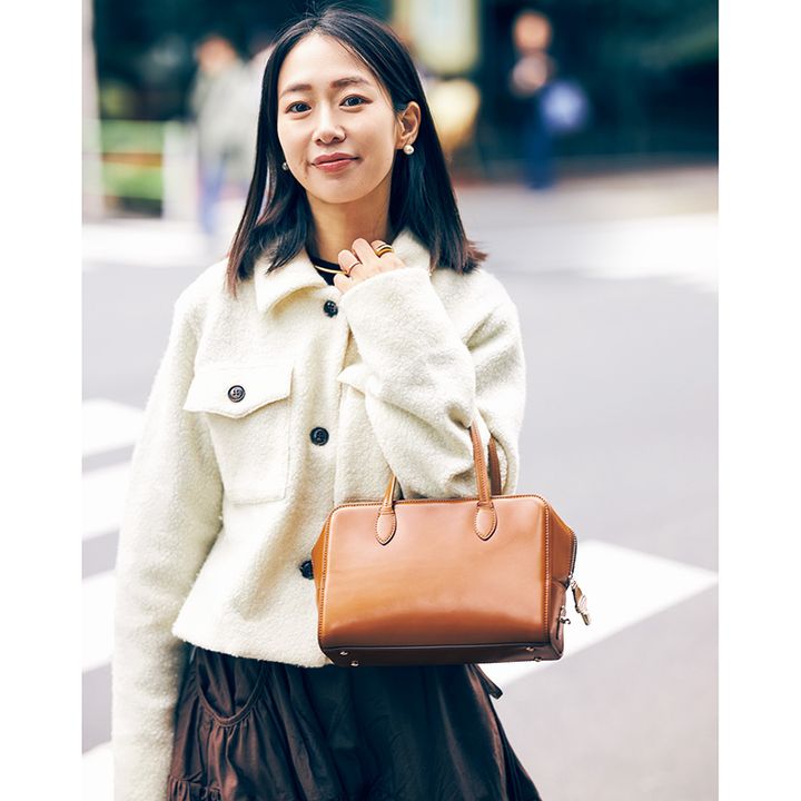 白のショート丈ジャケットとスカートのコーデにキャメル色の横長ボストンを持ったVERYライター