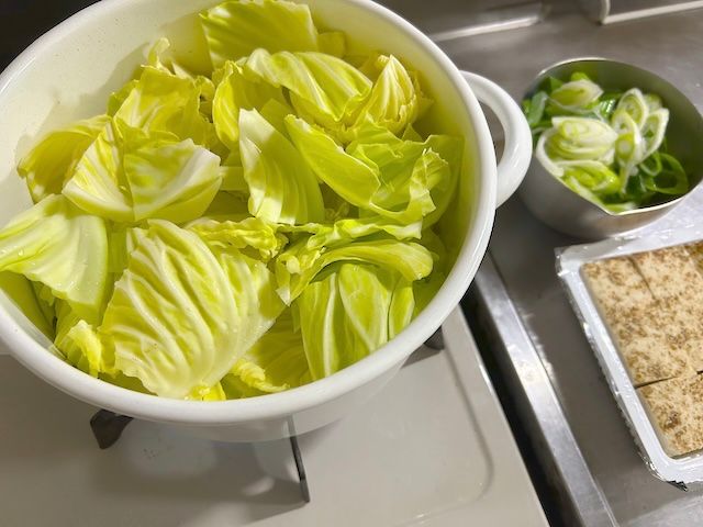 もつ鍋の調味料とキャベツ、水を入れた鍋と刻んだネギ、焼き豆腐。