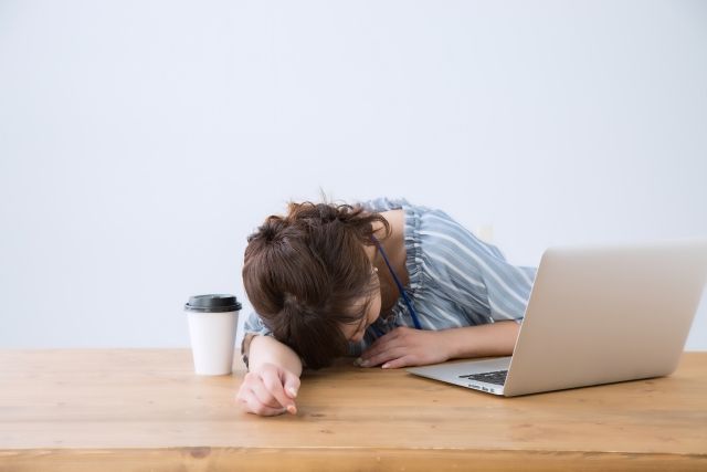 パソコンとコーヒーが乗る机の上で寝てしまっている会社員の女性