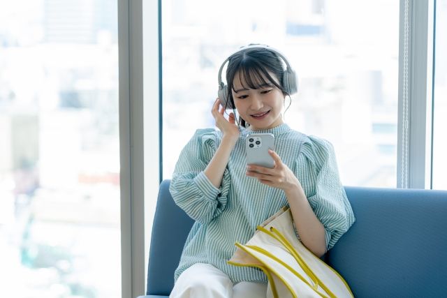 ソファに座ってヘッドフォンをつけて音楽を聴く女性