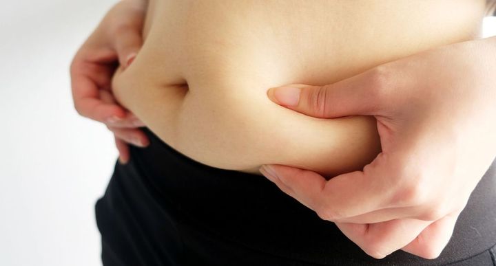 自身のぽっこりおなかをつまんでいる女性の手元