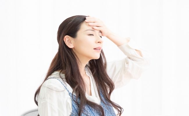 体調不良で額に手を当てている女性