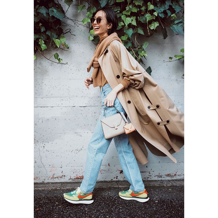 ベージュトレンチに同色ニットを肩掛け薄色デニムのコーデ