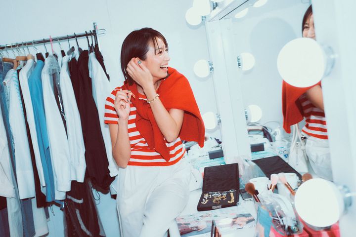 赤のボーダートップスと白パンツに赤のニットを肩掛けして楽屋で談笑する東原亜希さん