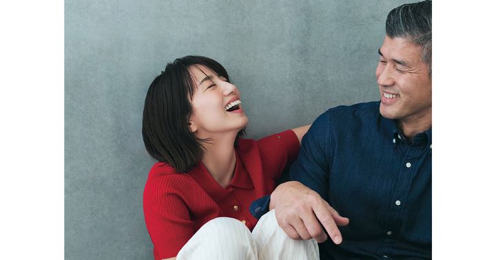 赤のポロニットと白のパンツを穿いて夫の井上康生さんの横で笑う東原亜希さん